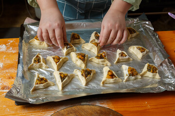 Women's hands put triangle gomentashi cookies on foil for baking for the holiday of Purim