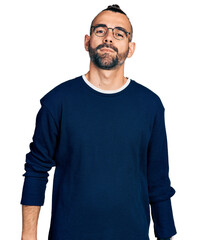 Hispanic man with ponytail wearing casual sweater and glasses relaxed with serious expression on...