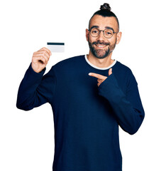 Hispanic man with ponytail holding credit card smiling happy pointing with hand and finger
