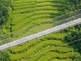 Aerial view of a Tibetan suspended bridge in Nepal is a primitive type of bridge in which the deck...