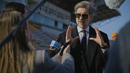 Interview of private investor at press conference for TV news. Organization representative answering press questions and giving interview outside a soccer stadium. Journalists crowd on press campaign.