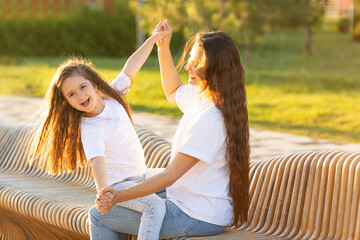 Happy mother having fun with her daughter outdoor - Family and love concept. Portrait of mother and daughter in the city park at summer sunset