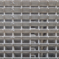 A large multi-storey apartment building is under construction, with a grey facade and a pattern of holes. Full-frame background. Low angle view,