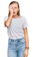 Beautiful young blonde woman wearing casual white t shirt yawning tired covering half face, eye and mouth with hand. face hurts in pain.