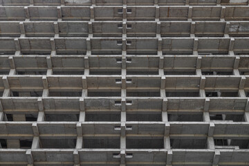 A large multi-storey apartment building is under construction, with a grey facade and a pattern of holes. Full-frame background. Low angle view,
