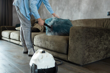 House cleaning. A man cleans the sofa and furniture with a steam generator. Cleaning service of the...