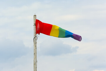 Wind flag with rainbow colors waving on a cloudy sky