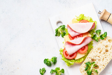 Fast food sandwich with lettuce, cheese, tomatoes and ham. Flat lay on white table.