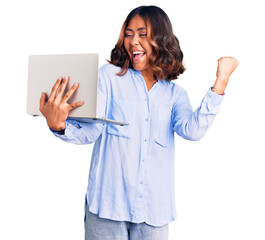 Young beautiful mixed race woman working using computer laptop screaming proud, celebrating victory...
