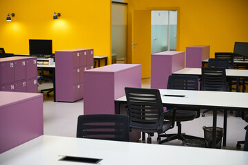 Call center with yellow walls and tables standing in lines