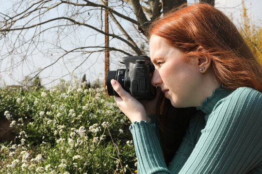 Red-haired woman taking photos of landscape flowers
