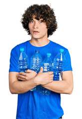 Caucasian teenager holding recycling plastic bottles in shock face, looking skeptical and...