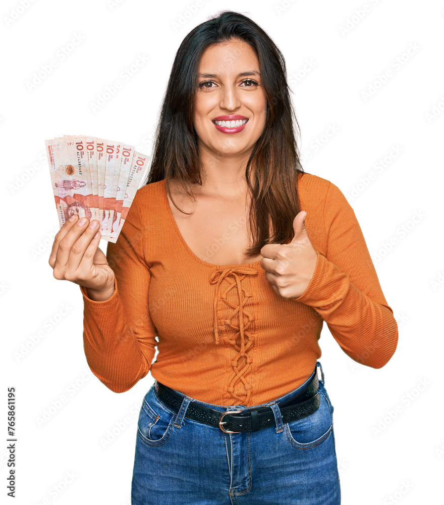 Sticker Beautiful hispanic woman holding 10 colombian pesos banknotes smiling happy and positive, thumb up doing excellent and approval sign