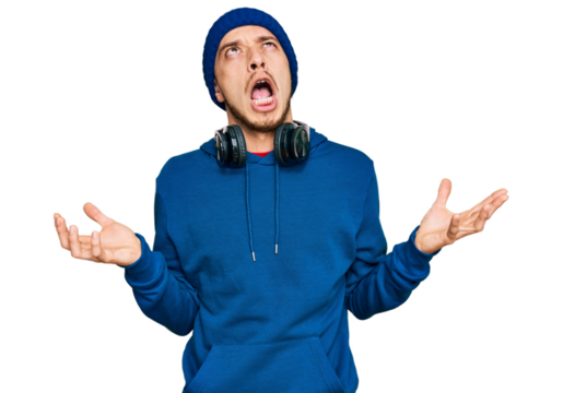 Hispanic young man wearing sweatshirt and wool hat crazy and mad shouting and yelling with aggressive expression and arms raised. frustration concept.