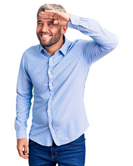 Young handsome blond man wearing elegant shirt very happy and smiling looking far away with hand...