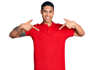 Young hispanic man wearing casual red t shirt looking confident with smile on face, pointing...