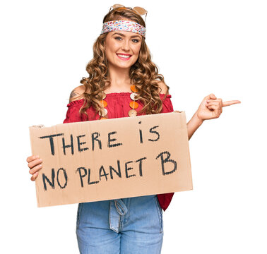 Young blonde girl wearing hippie style holding there is no planet b banner smiling happy pointing with hand and finger to the side