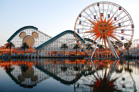 The Ferris Wheel, roller coaster and rides of Paradise Pier in Anaheim California are reflected in the lake