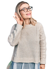 Young blonde woman wearing glasses smiling with hand over ear listening an hearing to rumor or gossip. deafness concept.