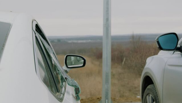 In dimly lit street car thief stealthily seizes backpack from car exploiting shattered glass. With each pilfered possession criminal's audacity grows leaving behind scene of disarray and loss.