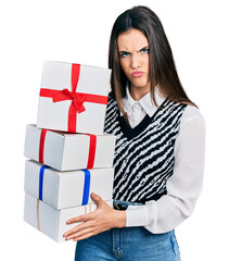 Young brunette teenager holding gifts skeptic and nervous, frowning upset because of problem. negative person.