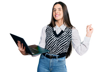 Young brunette teenager working using computer laptop screaming proud, celebrating victory and...