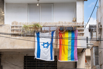 Rainbow LGBT flag and an Israeli flag hang from the balcony of an apartment building in Tel Aviv, Israel - obrazy, fototapety, plakaty