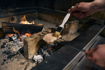 Partial chef smearing pike fillet with brush before frying in burning fire place