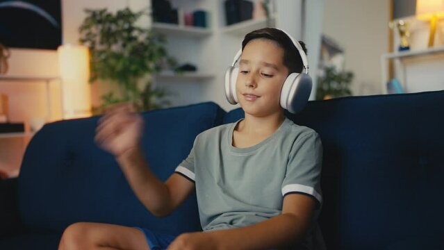 Happy boy in headphones beating imaginary drums with pencils, musical hobby