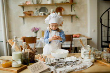 Girl cook 3 years old in a beautiful kitchen, in a chef's hat, in an apron, daylight