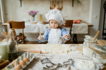 Girl cook 3 years old in a beautiful kitchen, in a chef's hat, in an apron, daylight