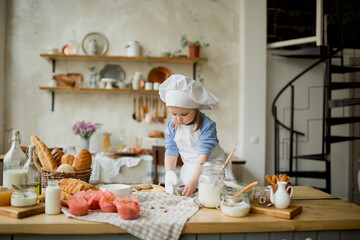 Girl cook 3 years old in a beautiful kitchen, in a chef's hat, in an apron, daylight