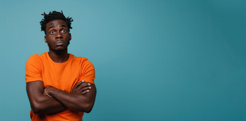 A man with dreadlocks and an orange shirt is staring at the camera. Portrait of a confused puzzled minded African American man in orange top isolated on blue background, copy space. - obrazy, fototapety, plakaty