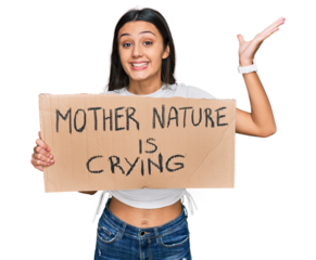 Young hispanic girl holding mother nature is crying protest cardboard banner celebrating victory with happy smile and winner expression with raised hands