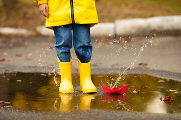 legs of child with rubber boots jump in puddle on an autumn walk. Happy child girl in a yellow...