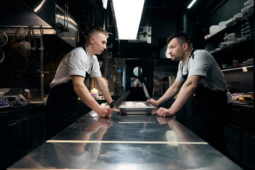 Two male competitor chefs with knives looking at each other in restaurant