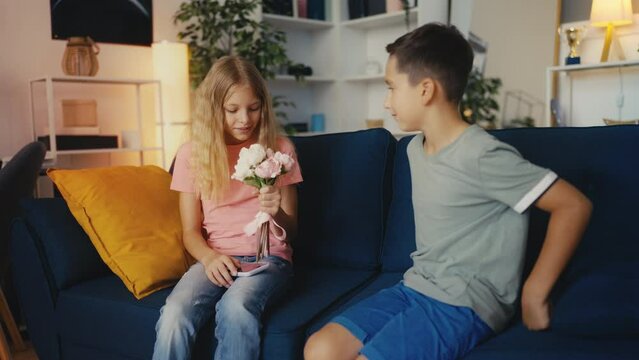 Shy pre-teen boy presenting flowers to a smiling girl, birthday greetings