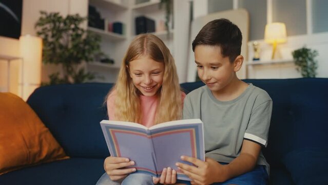 Cheerful girl and boy reading funny book together, friendship, hobby and rest