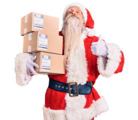Old senior man with grey hair and long beard wearing santa claus costume holding boxes smiling happy and positive, thumb up doing excellent and approval sign