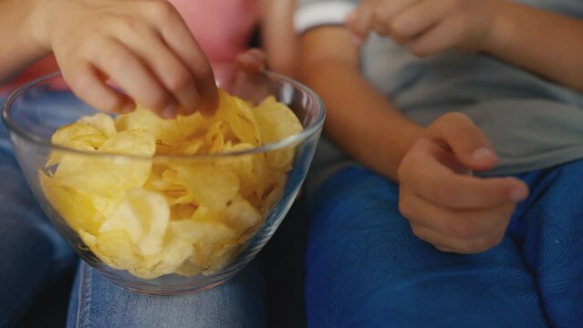 Close-up of kids eating potato chips while watching television, unhealthy snack