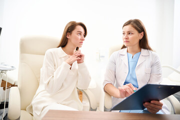 Female caucasian doctor showing to young tense woman her examining results