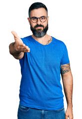 Fototapeta premium Hispanic man with beard wearing casual t shirt and glasses smiling friendly offering handshake as greeting and welcoming. successful business.