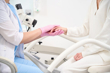 Side cropped of female gynecologist and woman patient holding hands in clinic