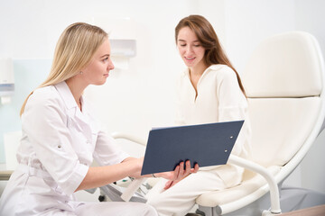 Female doctor showing to young focused woman her examining results in clinic
