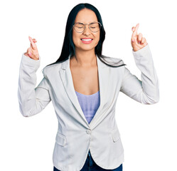 Beautiful hispanic woman with nose piercing wearing business jacket and glasses gesturing finger crossed smiling with hope and eyes closed. luck and superstitious concept.