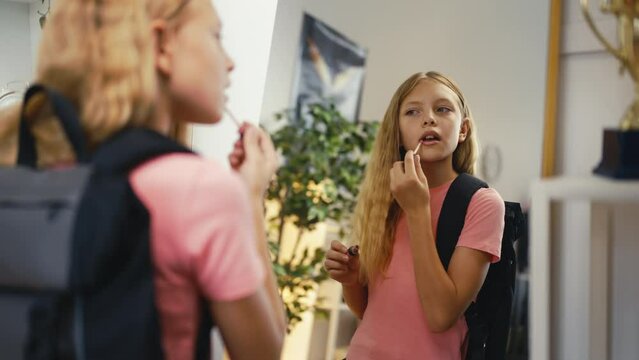 Adolescent girl applying lip gloss in front of mirror, getting ready for school