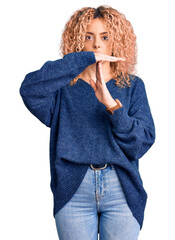 Young blonde woman with curly hair wearing casual winter sweater doing time out gesture with hands,...