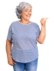 Senior woman with gray hair wearing casual striped clothes smiling with happy face looking and pointing to the side with thumb up.