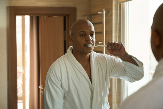Mirror reflection of young african american man brushing teeth in bathroom - Powered by Adobe