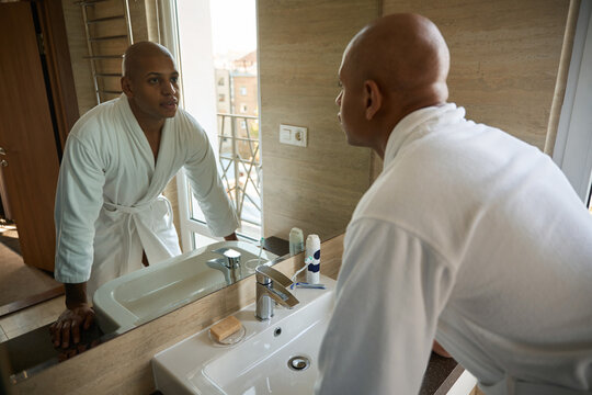 Young african american man looking at his face in mirror in bathroom at morning - Powered by Adobe